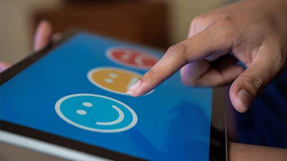 Person touching tablet with happy to unhappy smiley faces on