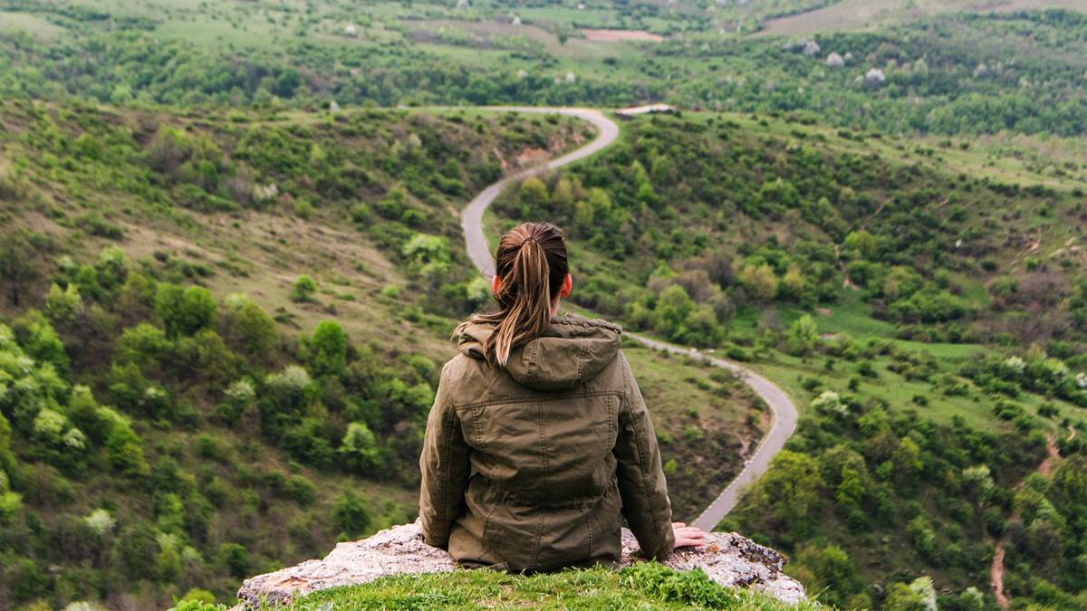 Young woman sitting on top of a hill, looking down on a mountain path