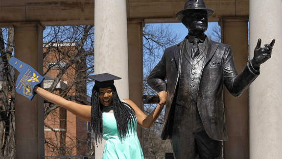 Photo of April posed with a statue on her campus, for her college graduation