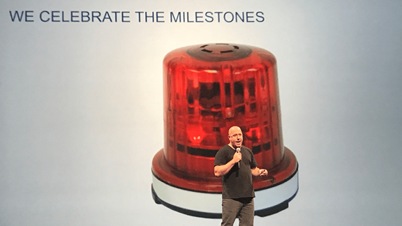 Mark Ardito as a speaker in front of a background that says "We celebrate the milestones"