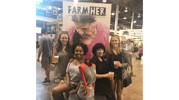 Andrea with a photo of her teammates in front of a sign that reads: FarmHER