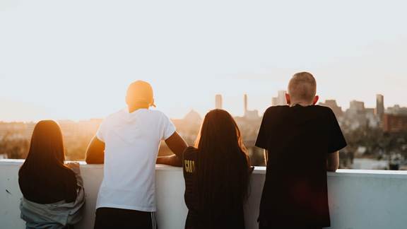 four young adults looking over a balcony at a sunset