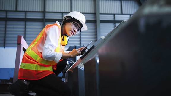 Female amazon partner wearing safety vest and hard hat looks at tablet in warehouse