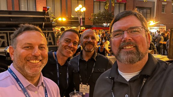 Four men smiling at the camera with a crowd behind