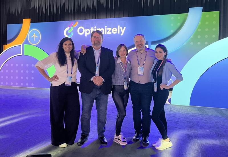 5 people on the stage smiling with Optimizely logo behind them