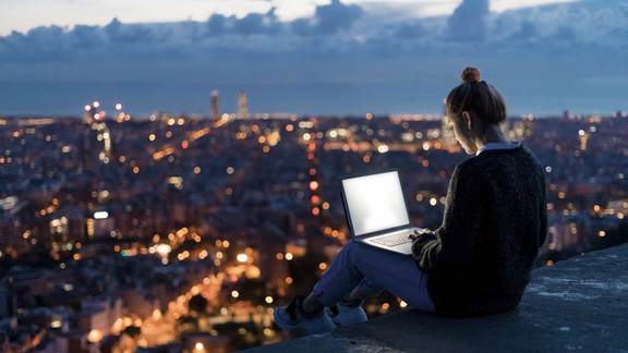 Young woman using a laptop with a city view during sunset